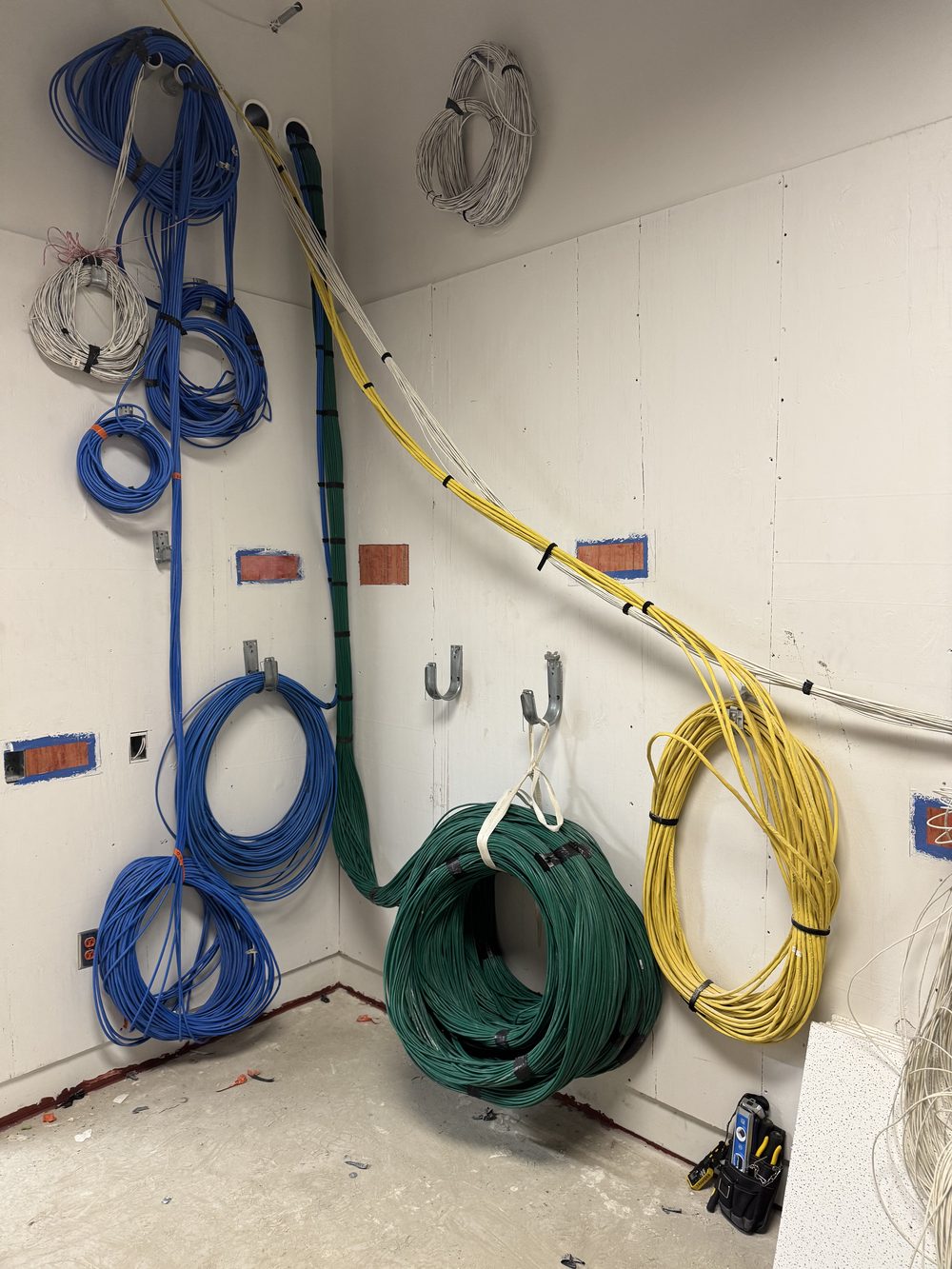 Colour-coded cable bundles coiled and hung on J-hooks during a cable plant install, with firestop patches on the wall